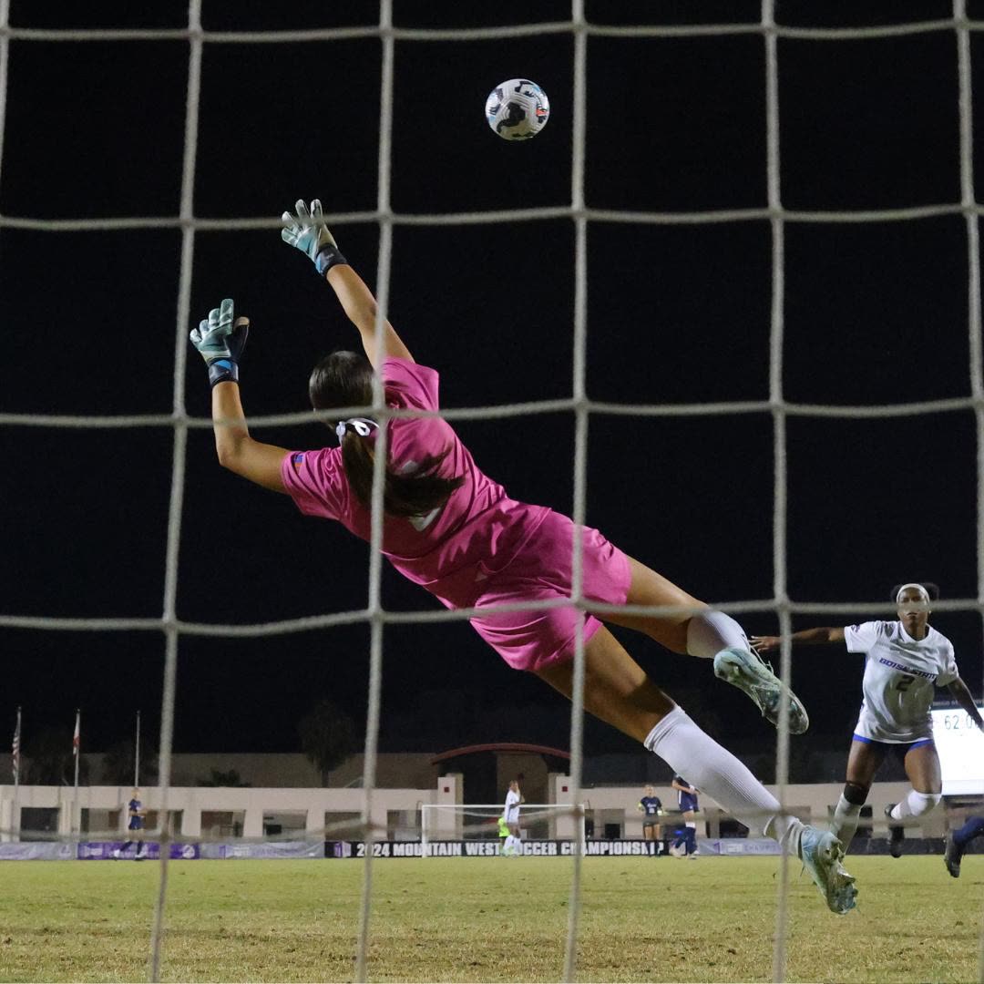 A youth goalkeeper dives for a save during a night game